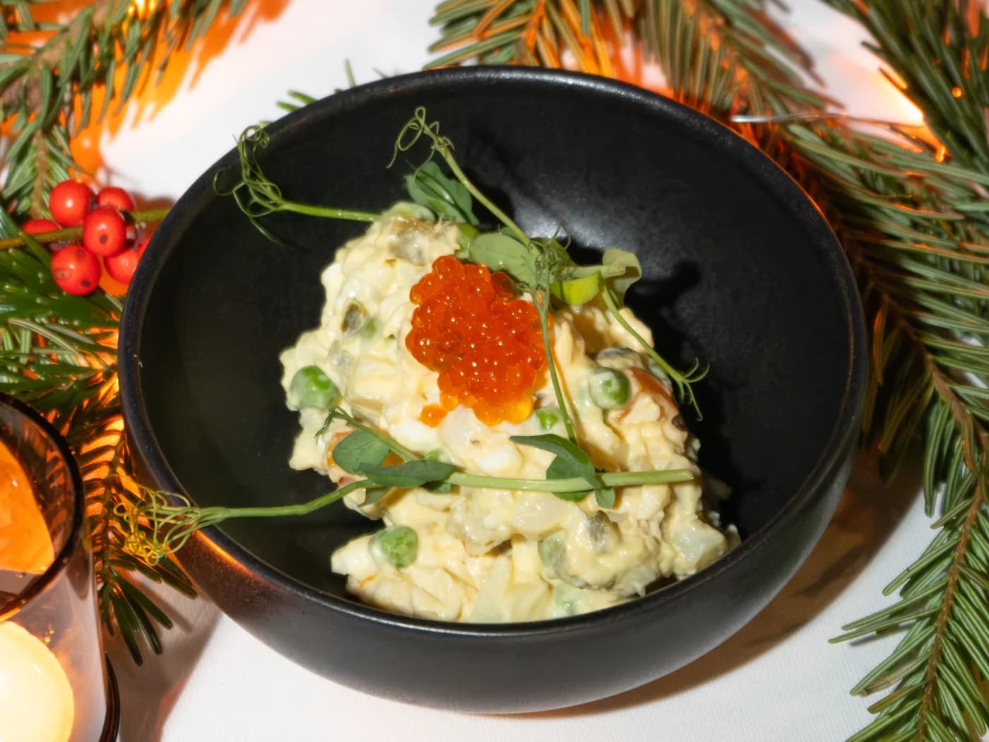 Olivier salad with salmon roe in a black bowl, dressed with fir